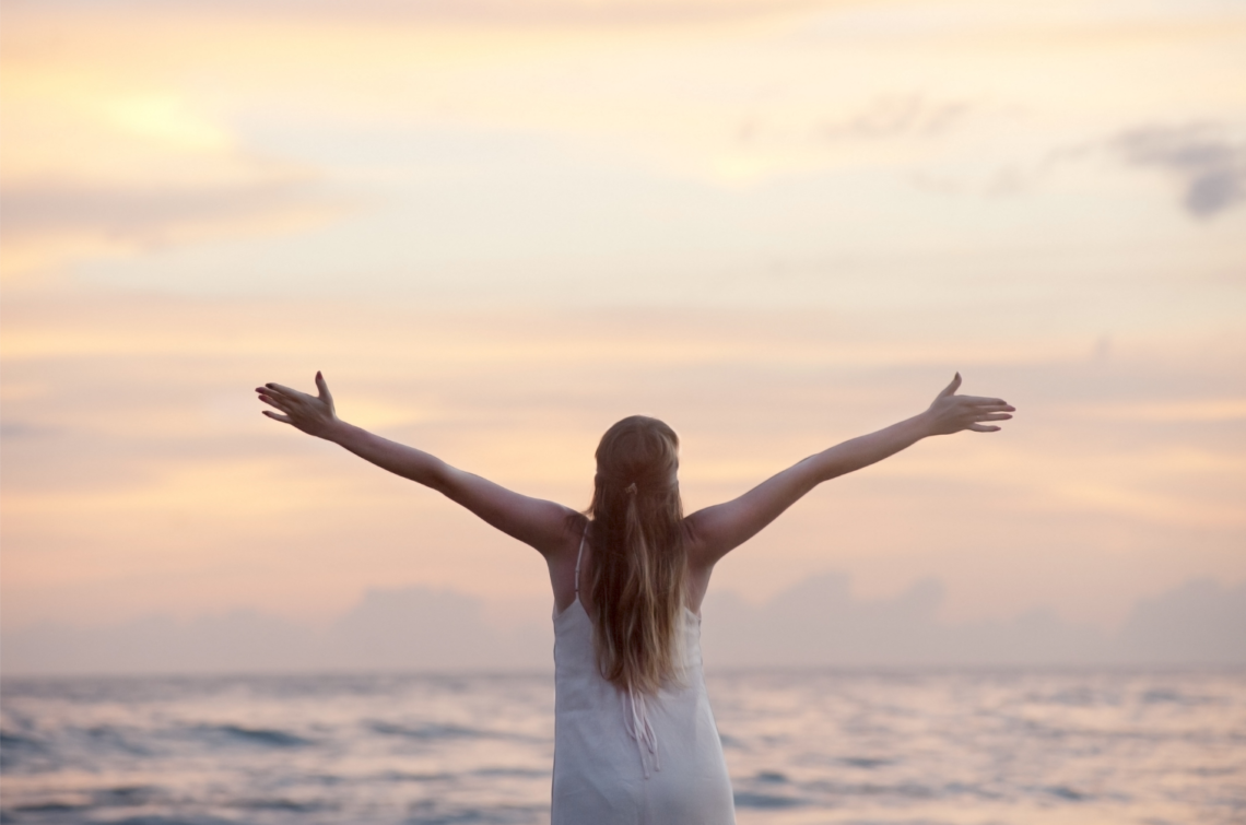 girl facing the ocean, hands reaching out