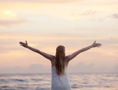 girl facing the ocean, hands reaching out